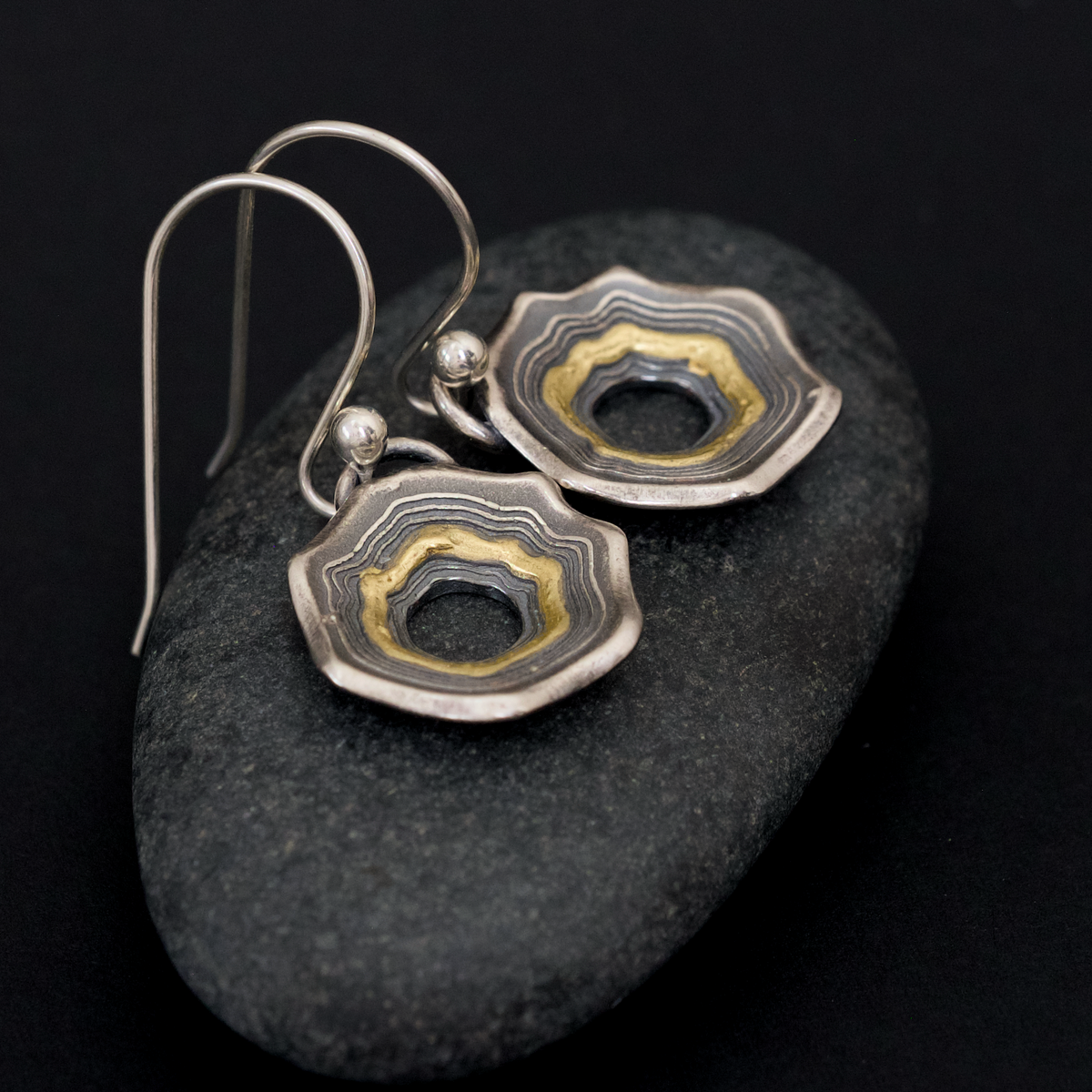 Pair of Pretty Good Year earrings resting on a dark river stone