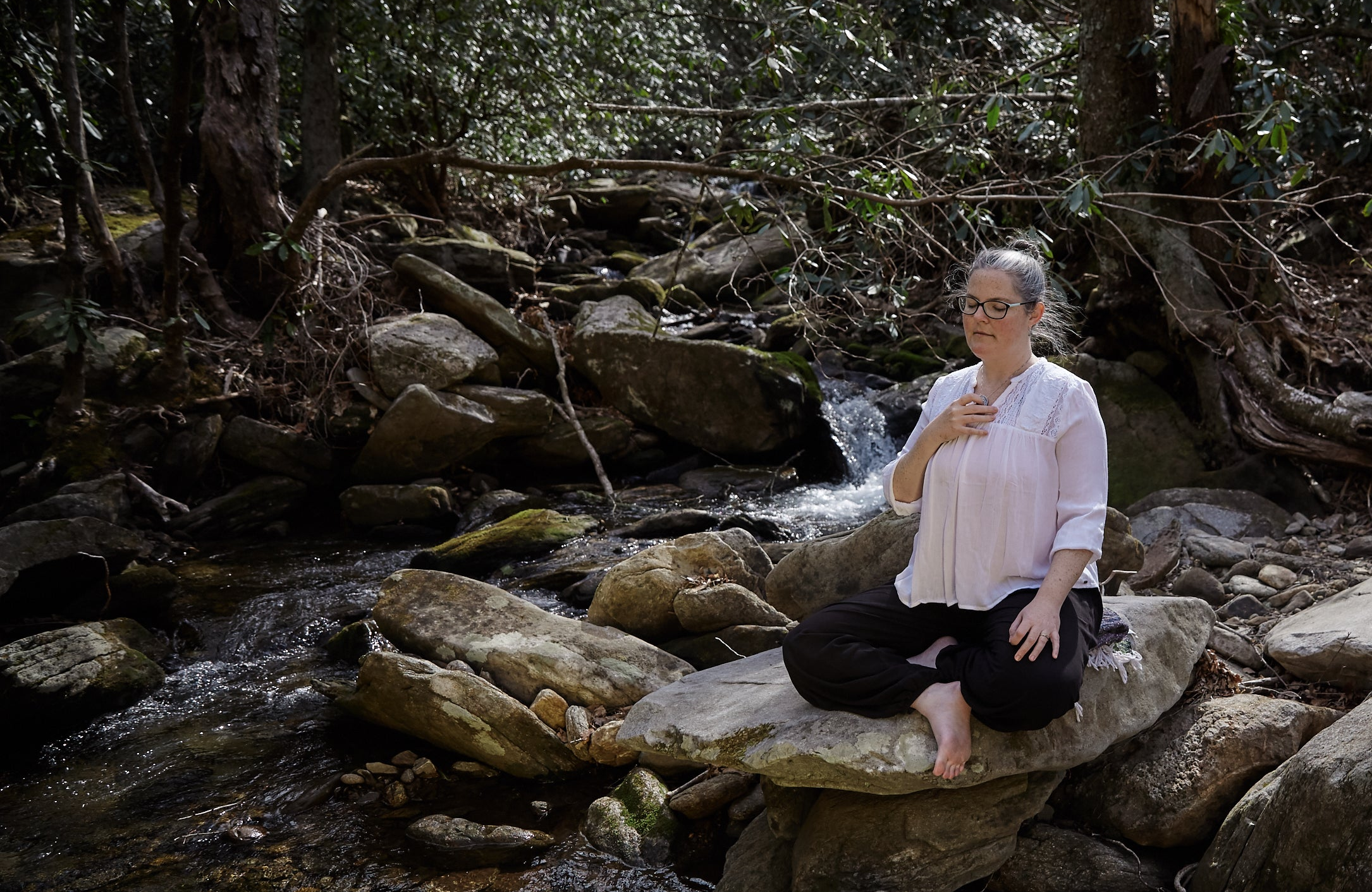 woman meditating by a steam in the forest holding a Centering Pendant
