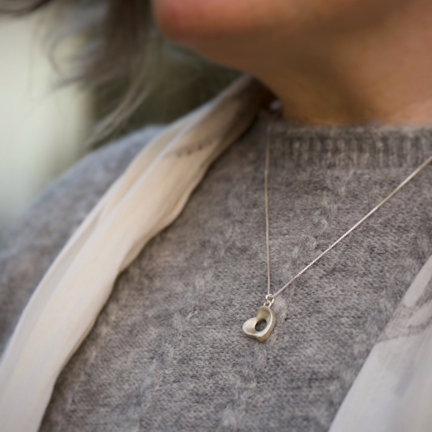 Close-up of a person wearing a necklace with a heart-shaped pendant.