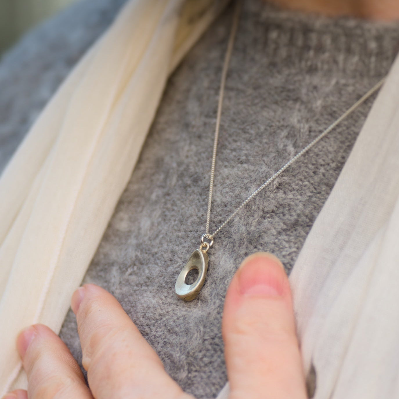 Hand near a delicate necklace with a small teardrop shaped pendant